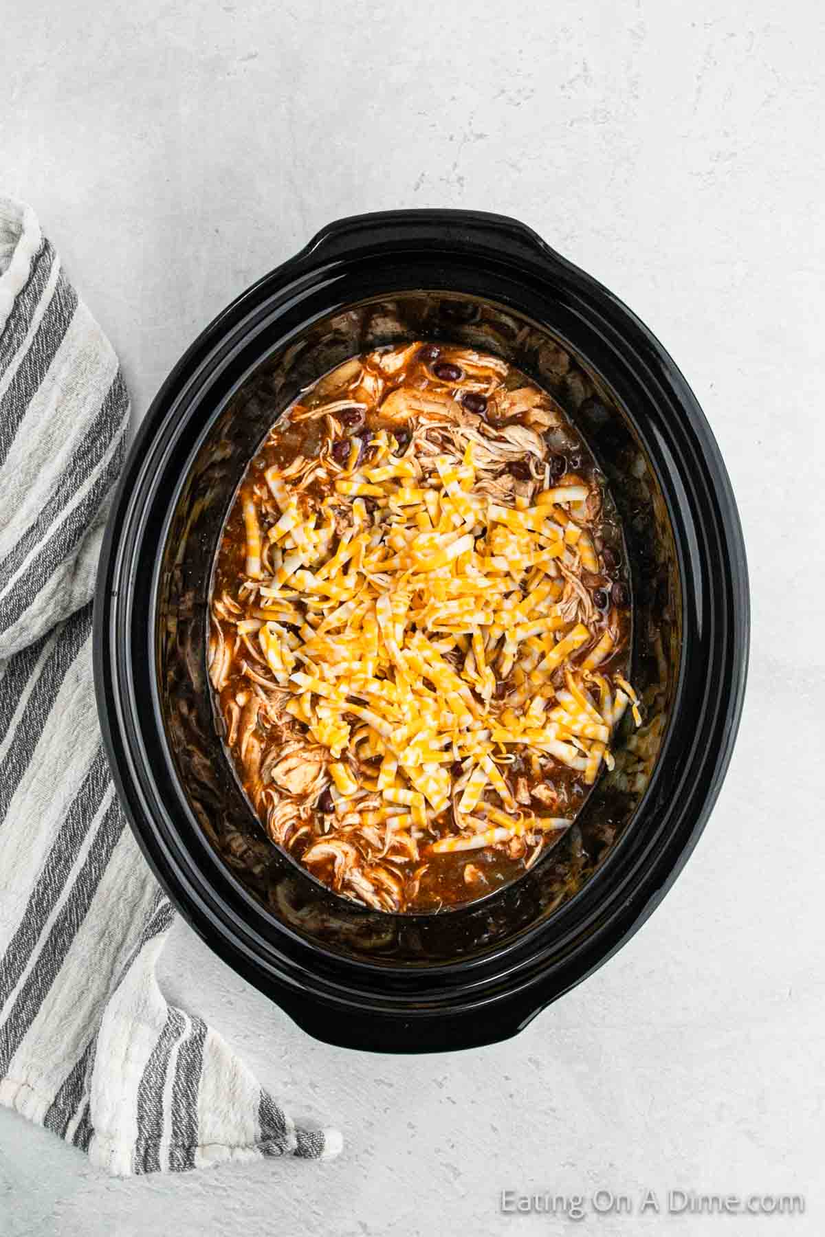 Shredded chicken topped with shredded cheese with the enchilada sauce in the slow cooker