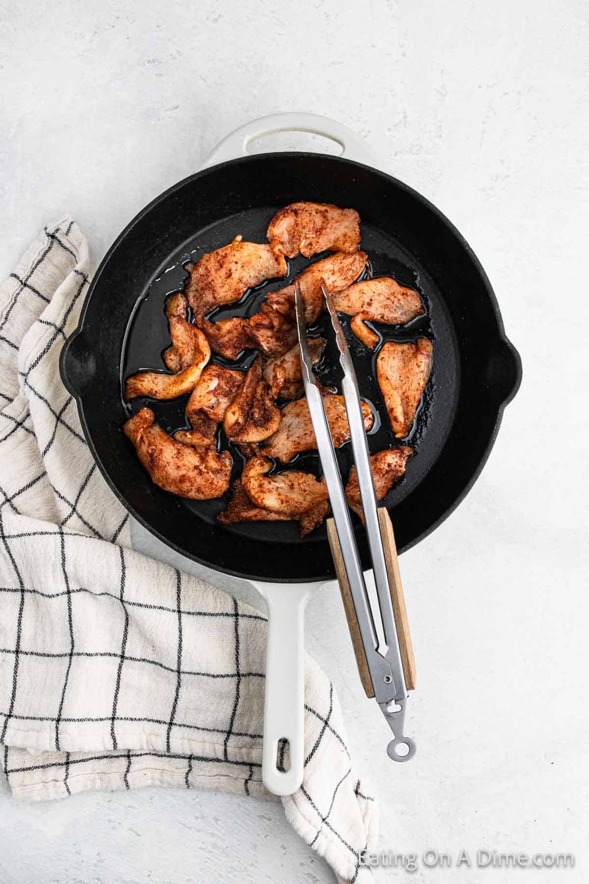 Cooking seasoned chicken strips in a cast iron skillet with tongs