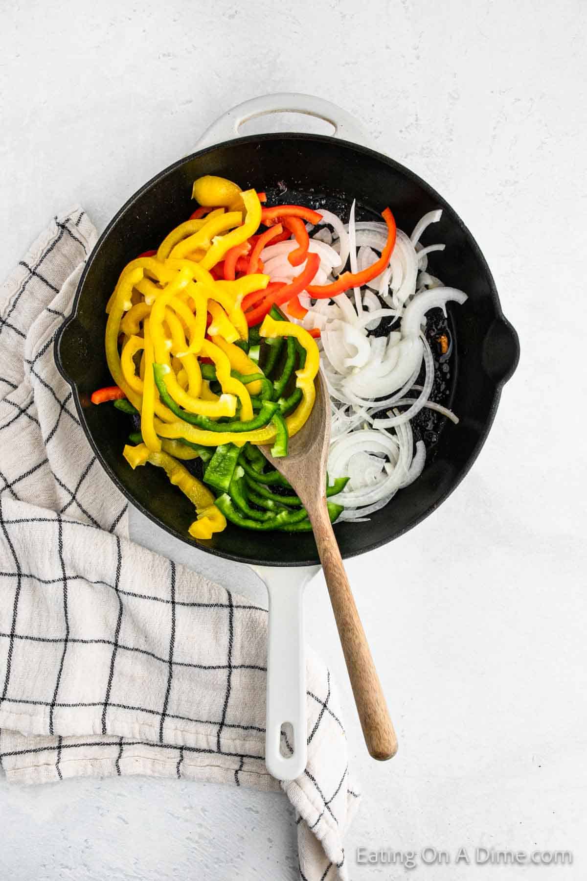 Yellow, red, green bell peppers and onion in a cast iron skillet with a wooden spoon