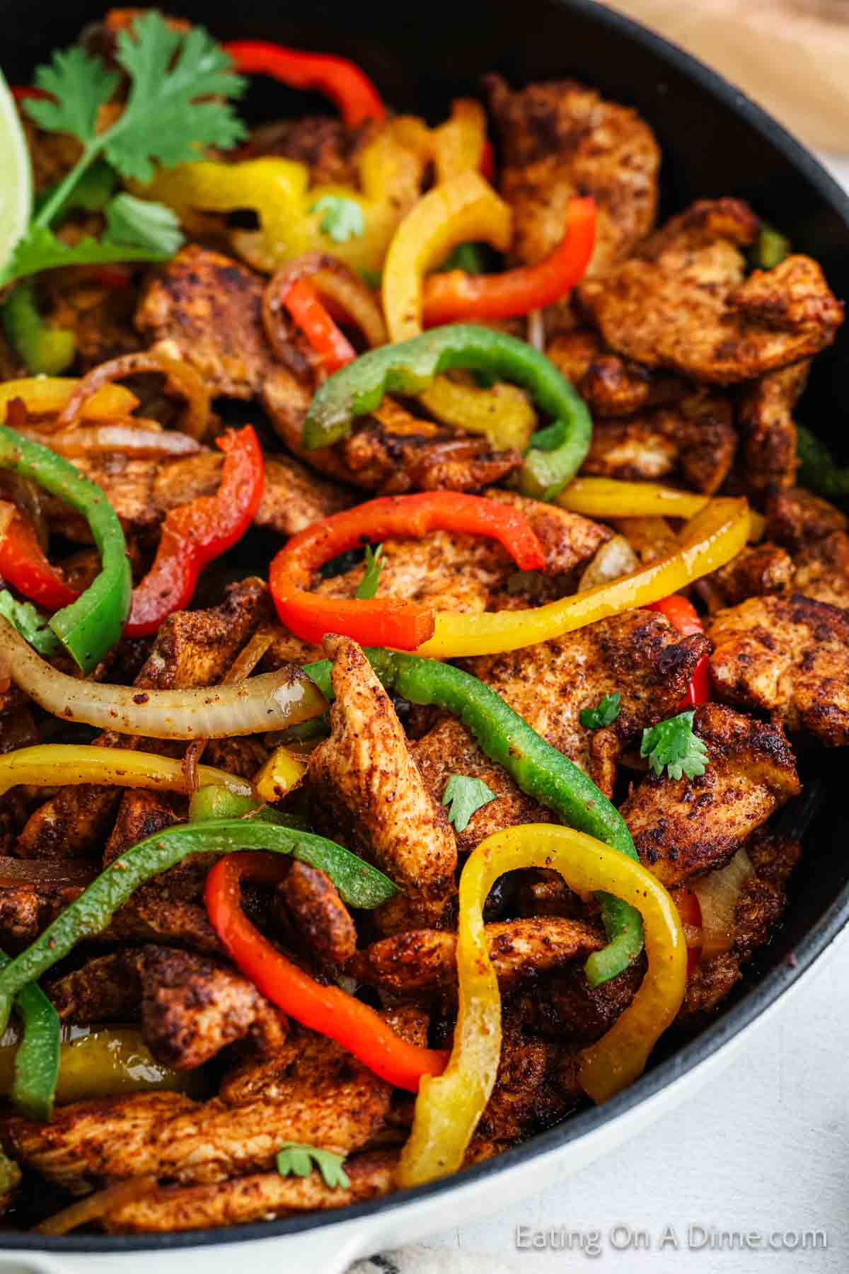 Strips of chicken fajita meat in a cast iron skillet with red, yellow, green bell peppers with onions