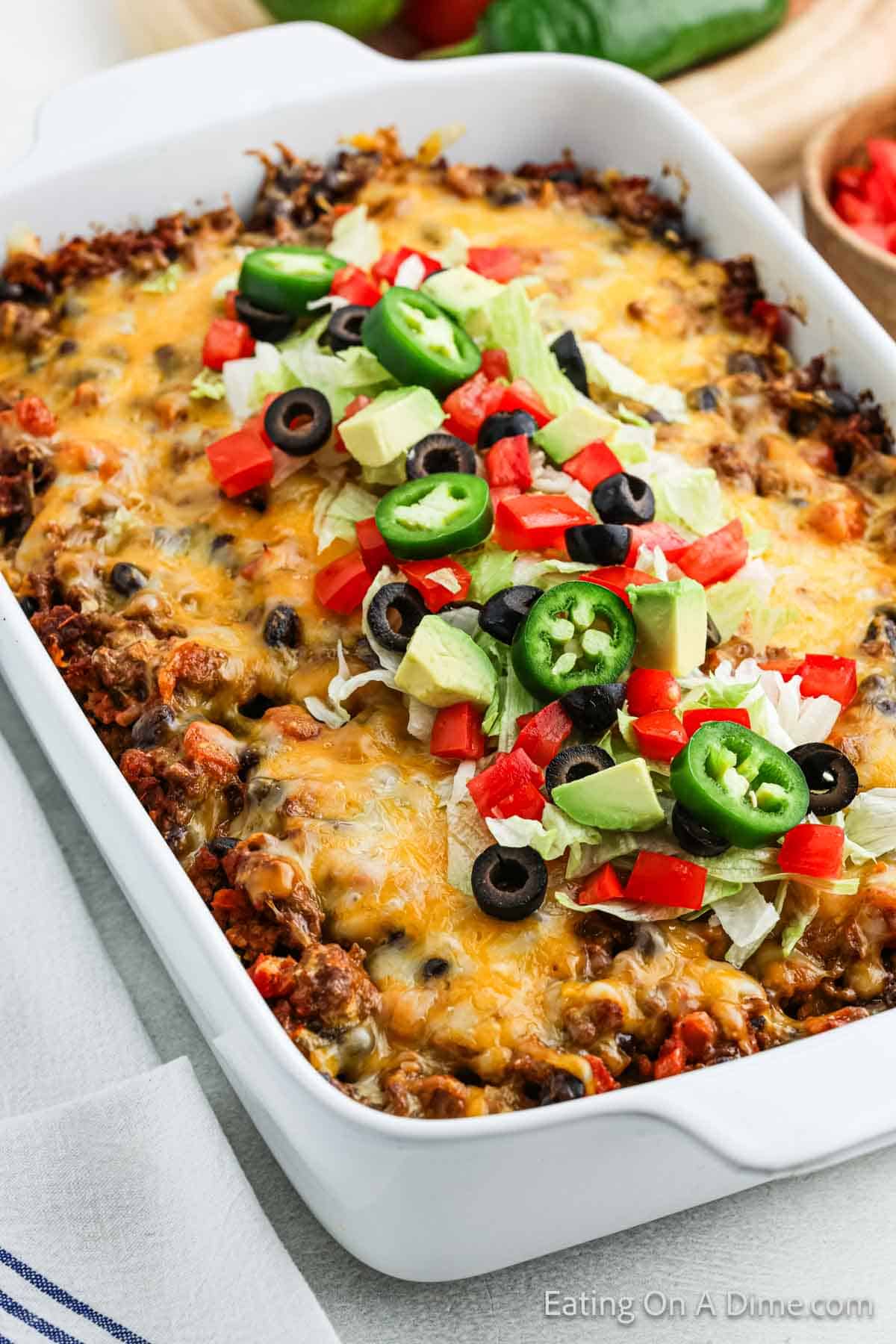 Taco Casserole in a baking dish topped with slice jalapeno peppers, diced tomatoes and avocado