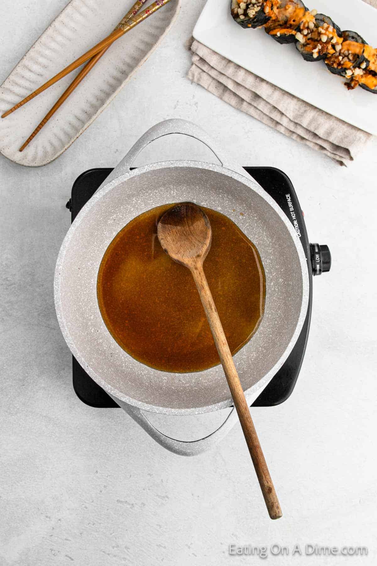 Heating rice vinegar, sugar, salt, and soy sauce in a large saucepan with a wooden spoon