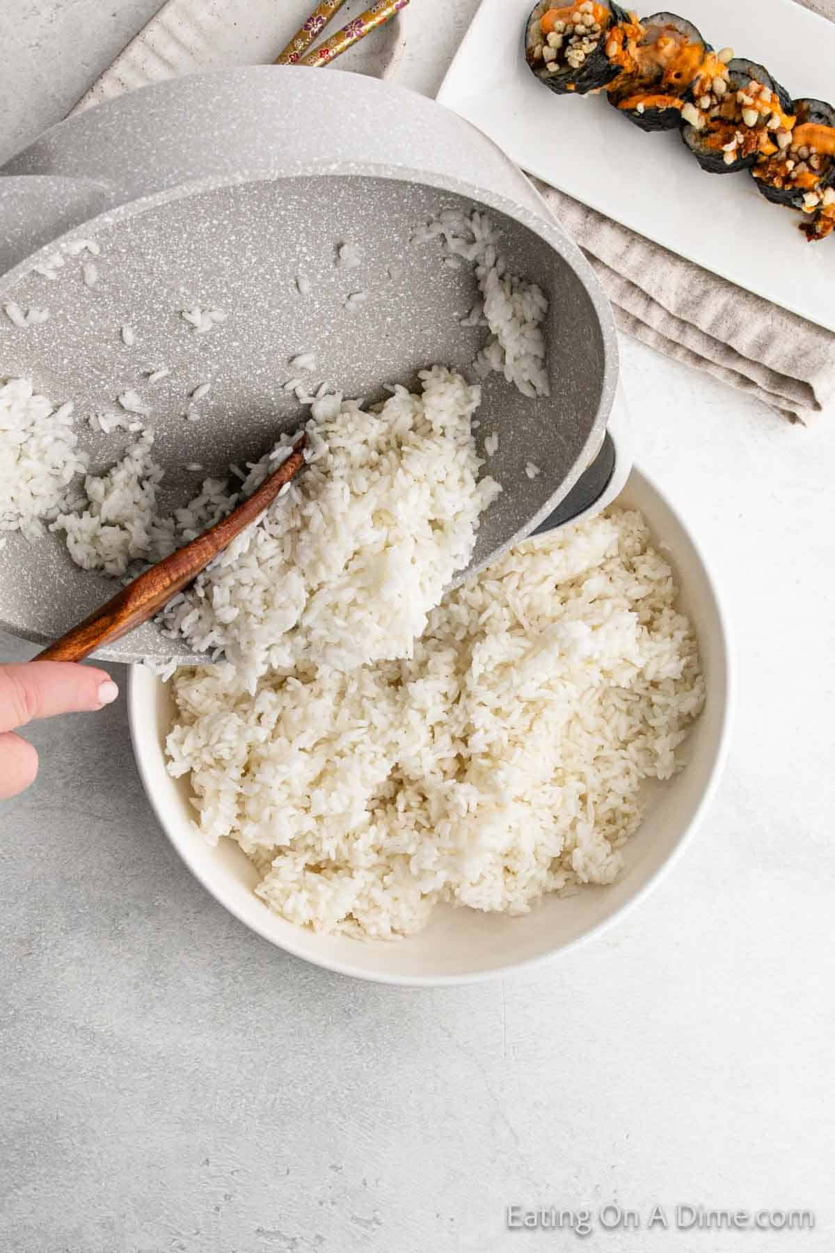 Pouring the white rice in a large bowl with the saucepan with a wooden spoon