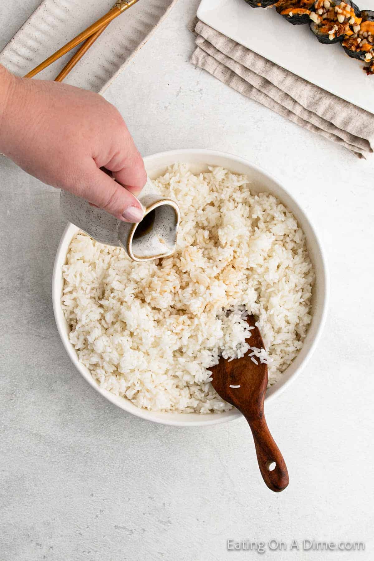 Drizzling vinegar mixture over the cooked white rice in a bowl with a wooden spoon