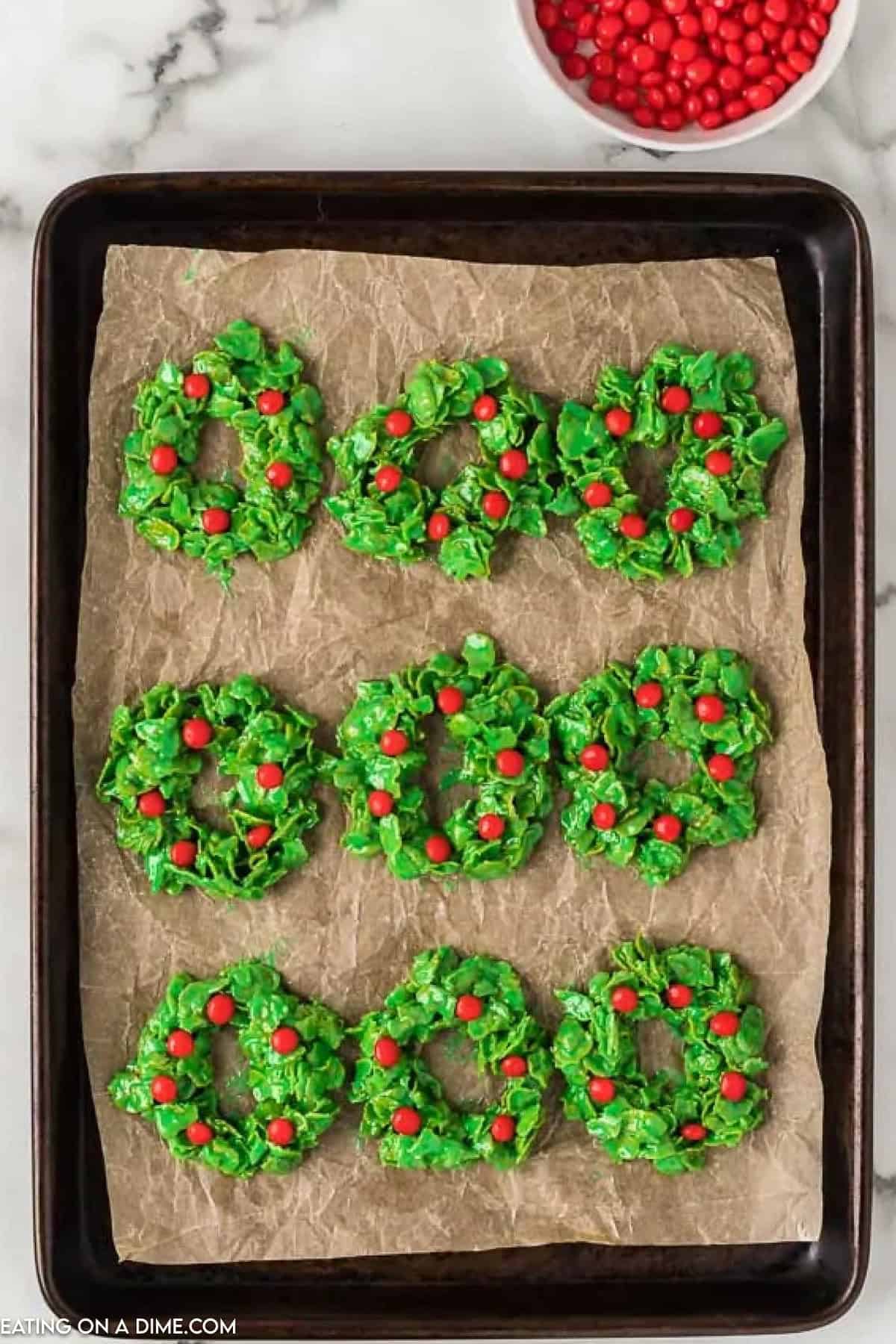 Christmas Wreath Cookies topped with red candy on a baking sheet lined with parchment paper