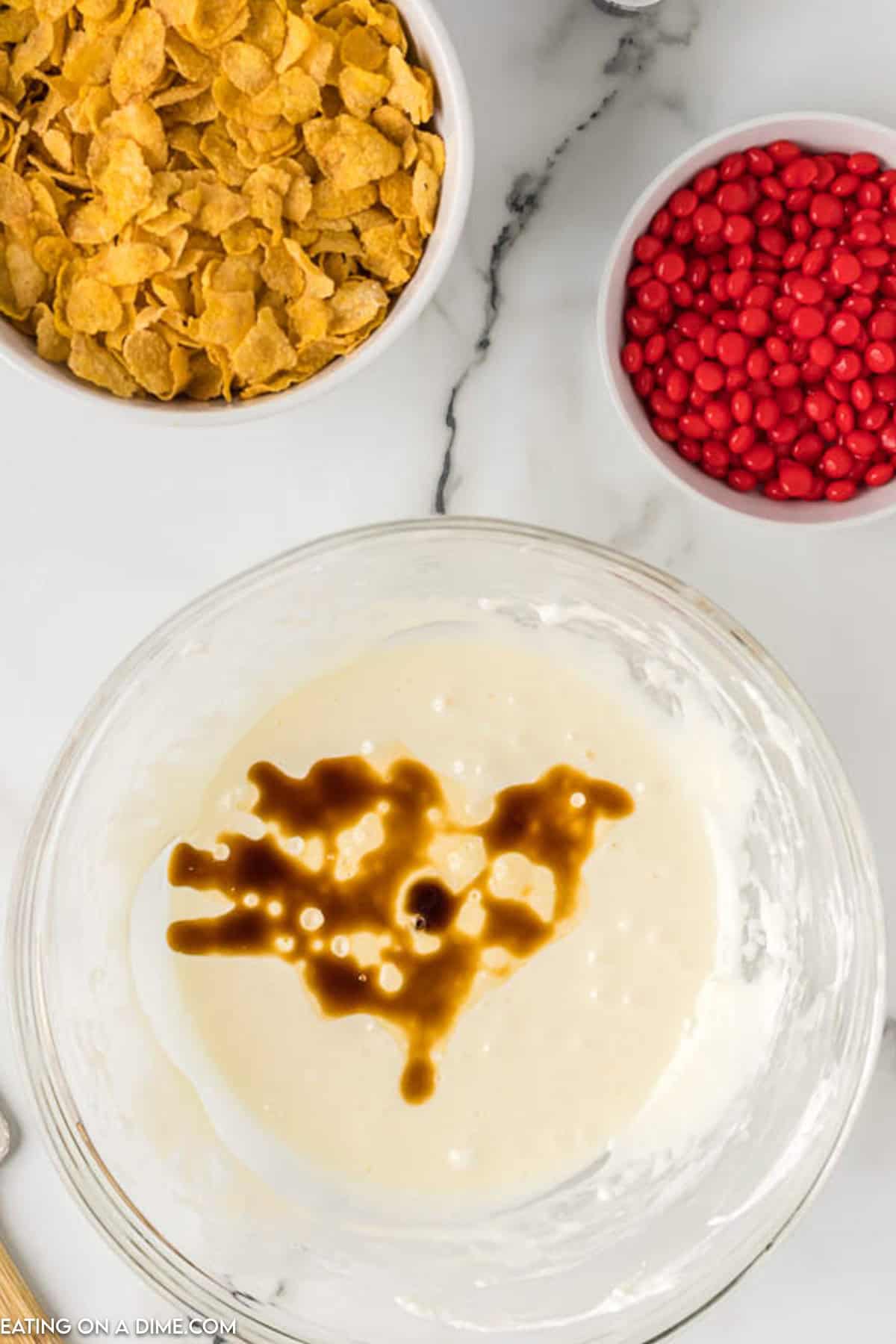 Melted marshmallow in a bowl with vanilla extract added to the mixture and a bowl of corn flakes on the side