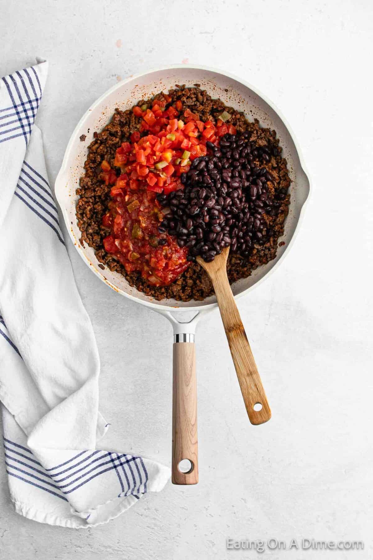 Topping the ground beef mixture in the skillet with black beans and diced tomatoes