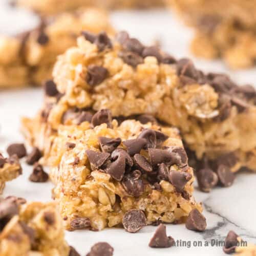 Close-up of homemade granola bars topped with chocolate chips on a marble surface, perfect for any meal plan. The bars have a rustic texture, with oats and chocolate pieces visible throughout. Additional chocolate chips are scattered around the bars.