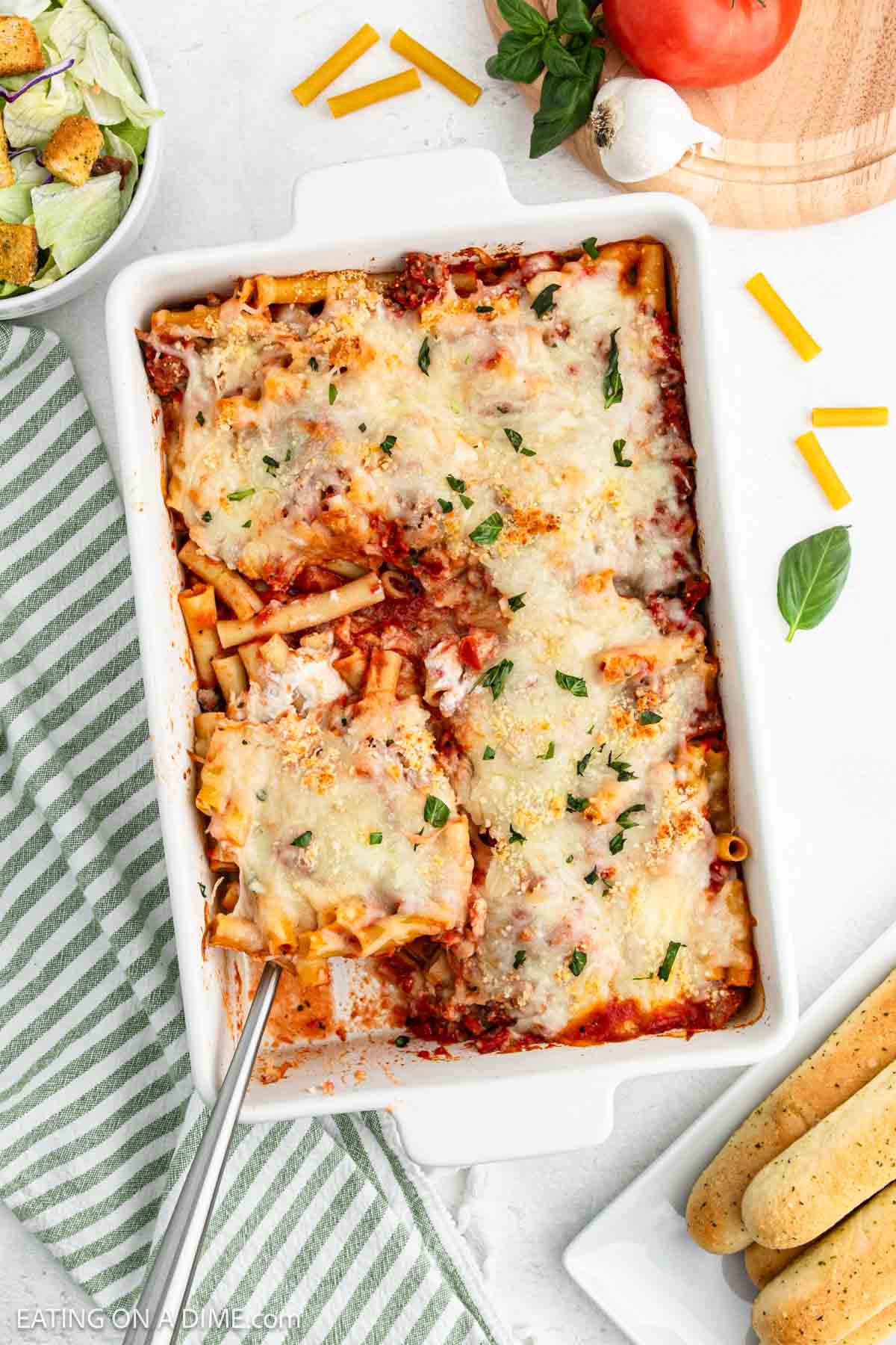 Baked Ziti in a baking dish topped with melted cheese and chopped basil