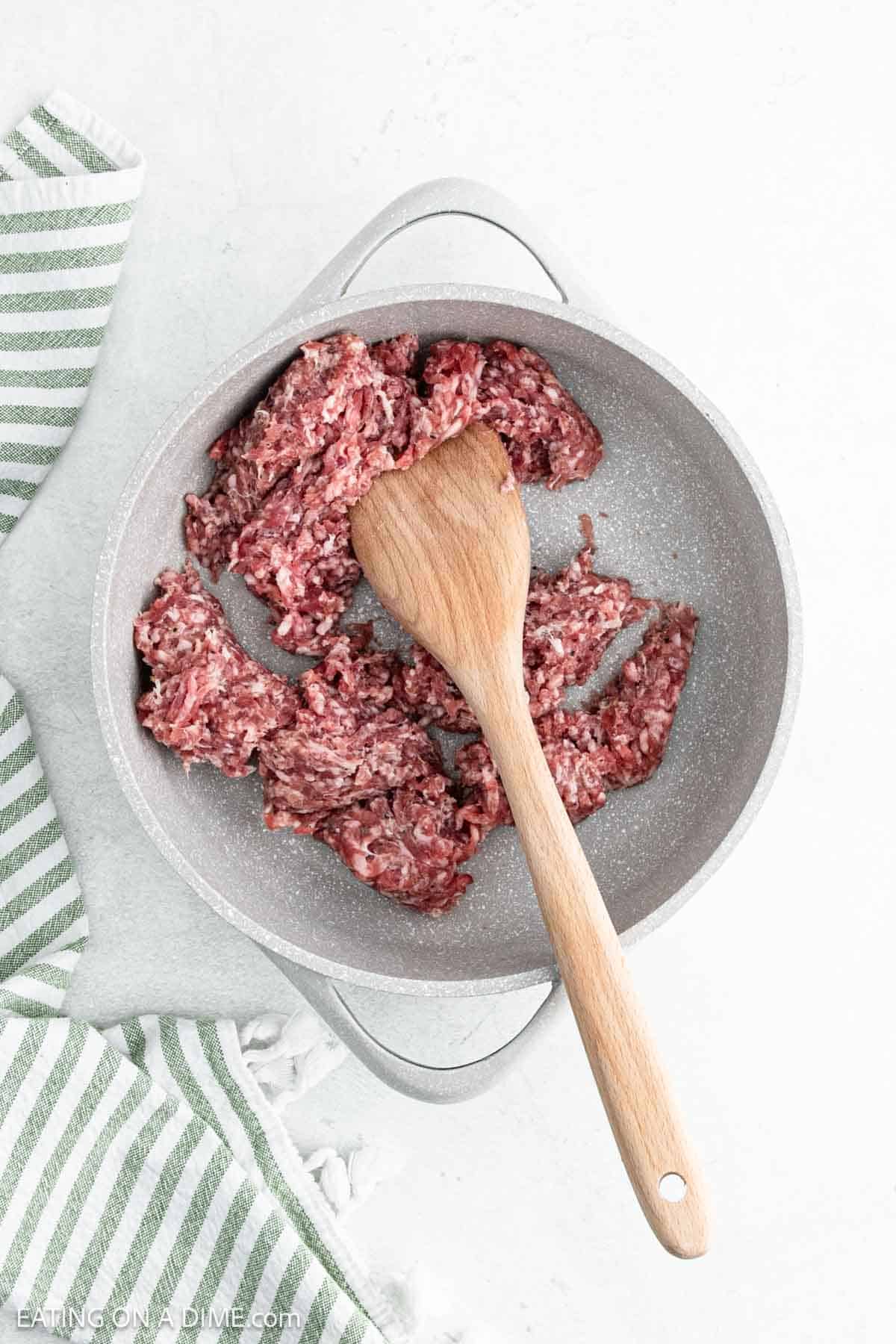 Cooking ground sausage in a large skillet with a wooden spoon