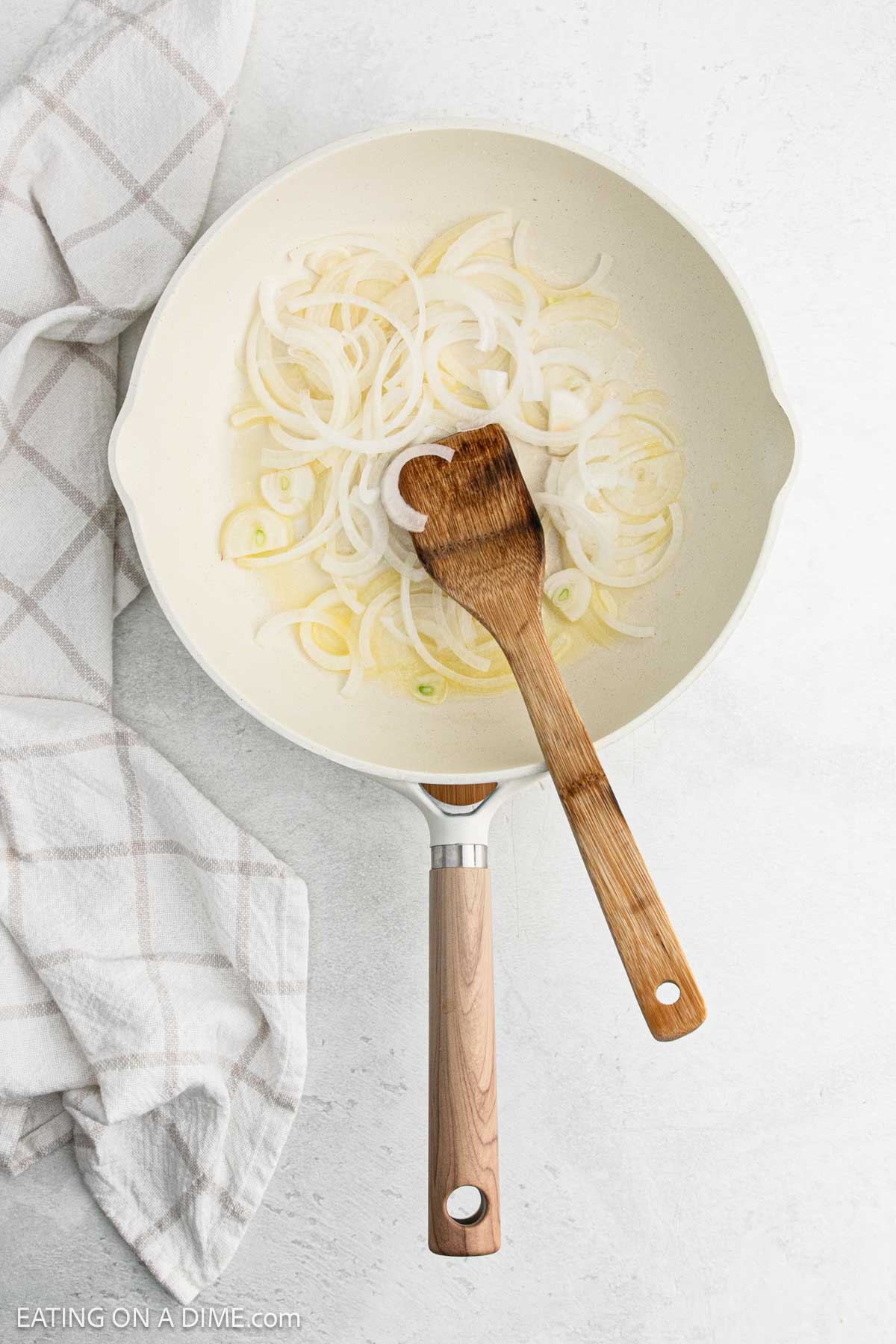 Cooked onions in a skillet with melted  butter and a wooden spoon