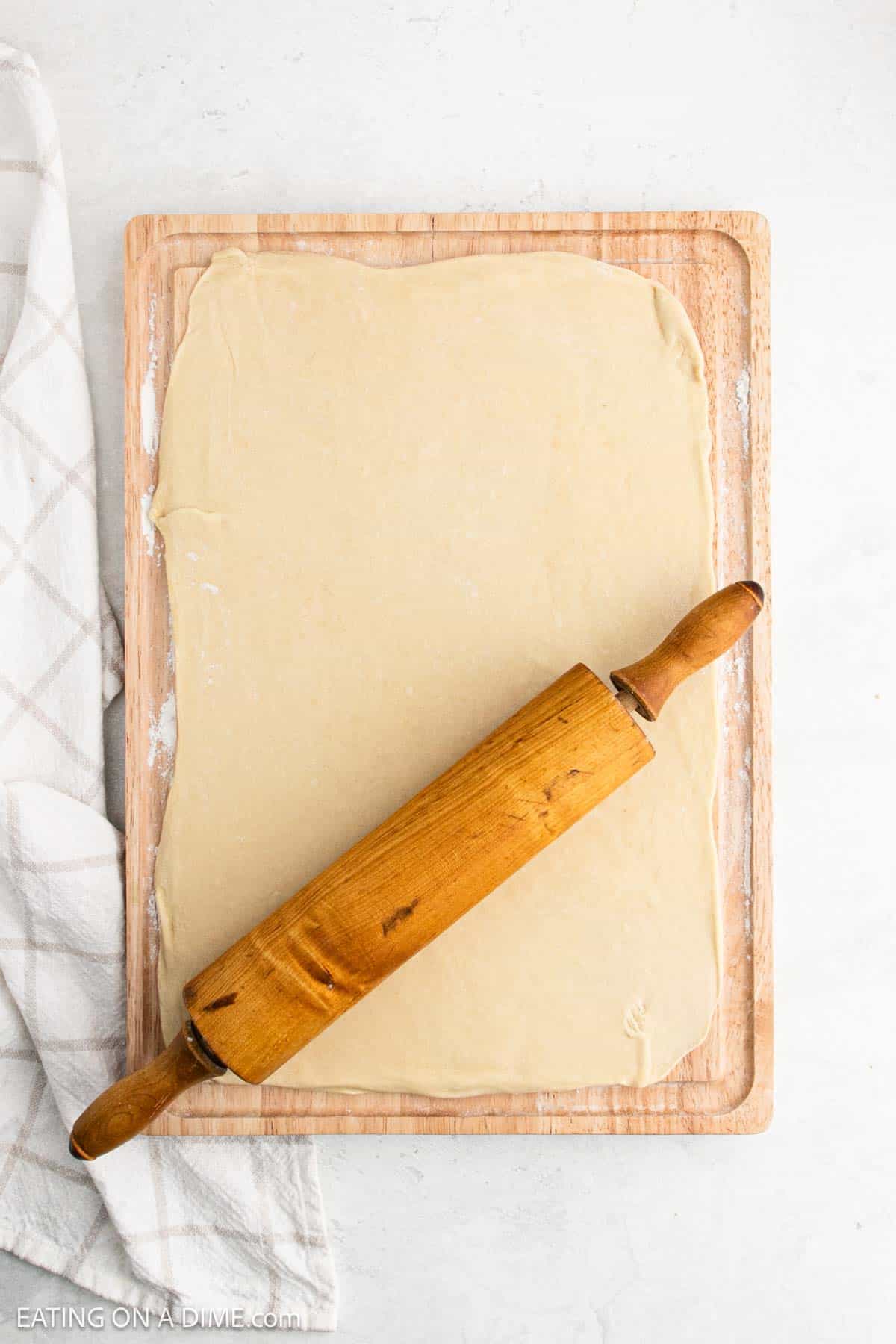 Dough spread onto a cutting board with a rolling pin on top