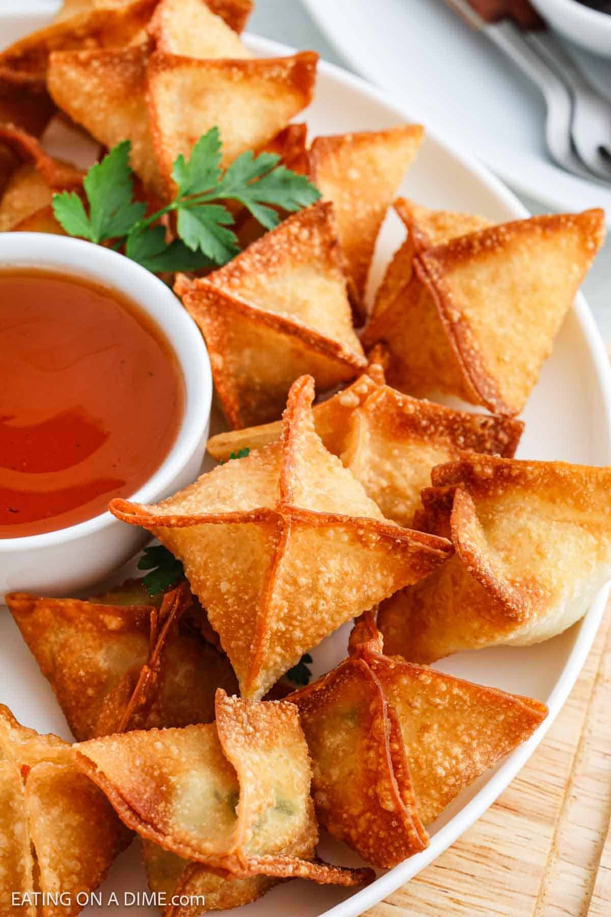 Golden Brown Crab Rangoon stacked on a platter with a bowl of dipping sauce