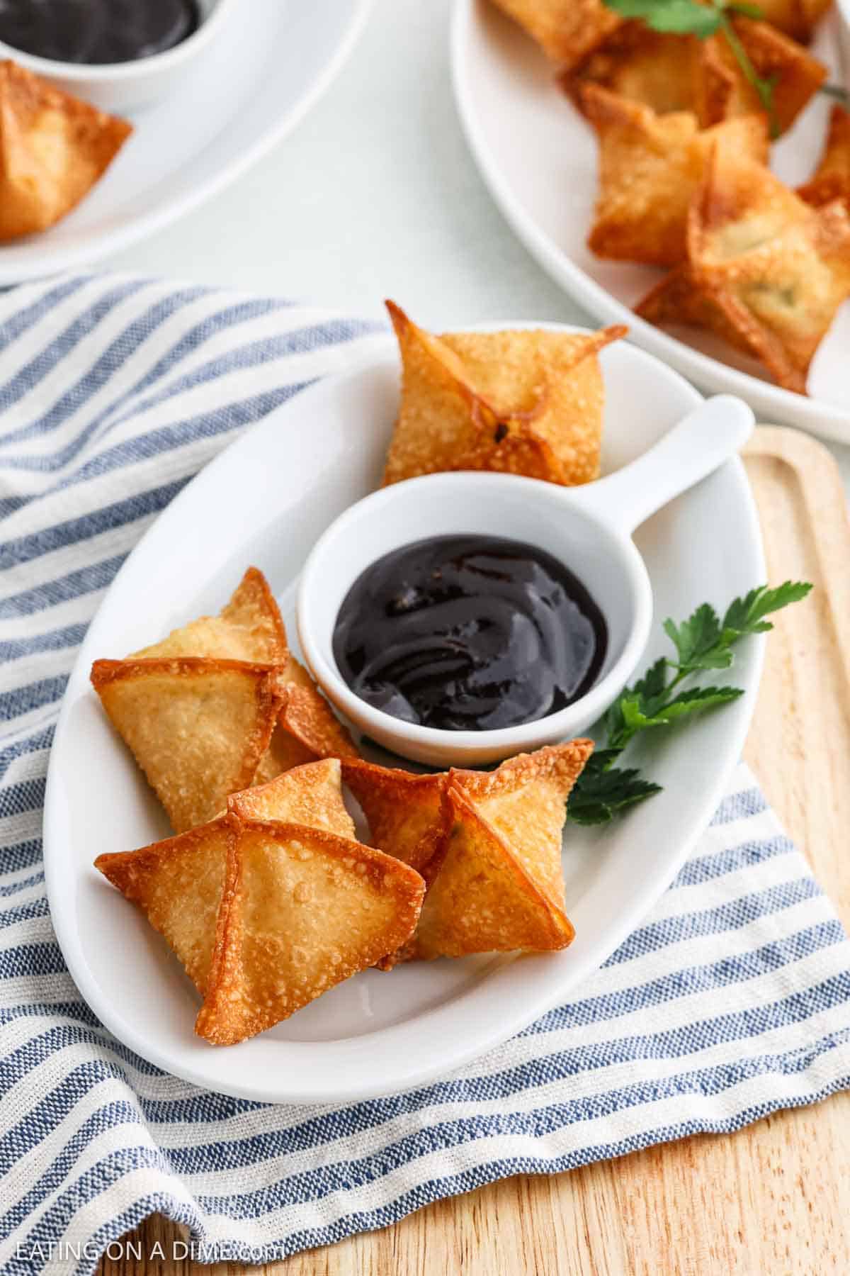 Crab Rangoon on a platter with a bowl of dipping sauce 