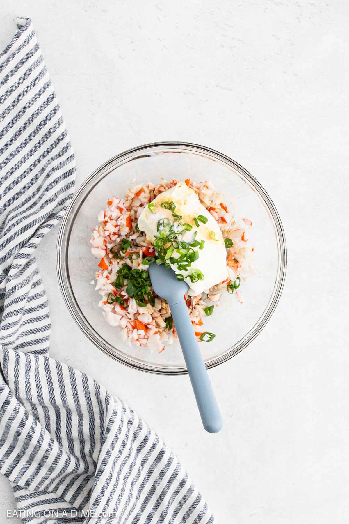 Crab meat mixed with green onions, cream cheese and other spices in a bowl with a spatula