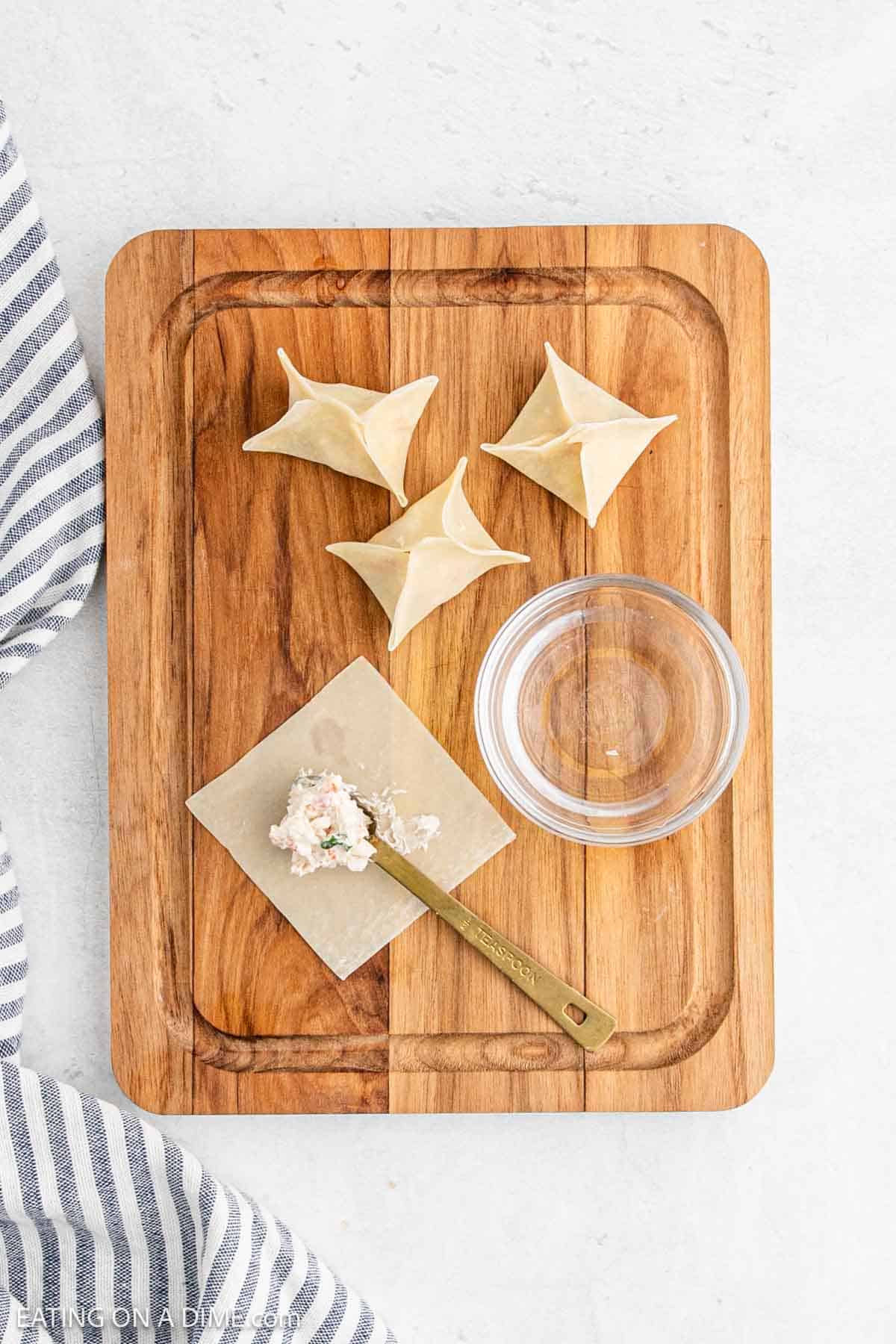 Filling the wonton wrappers with crab meat filling on a cutting board