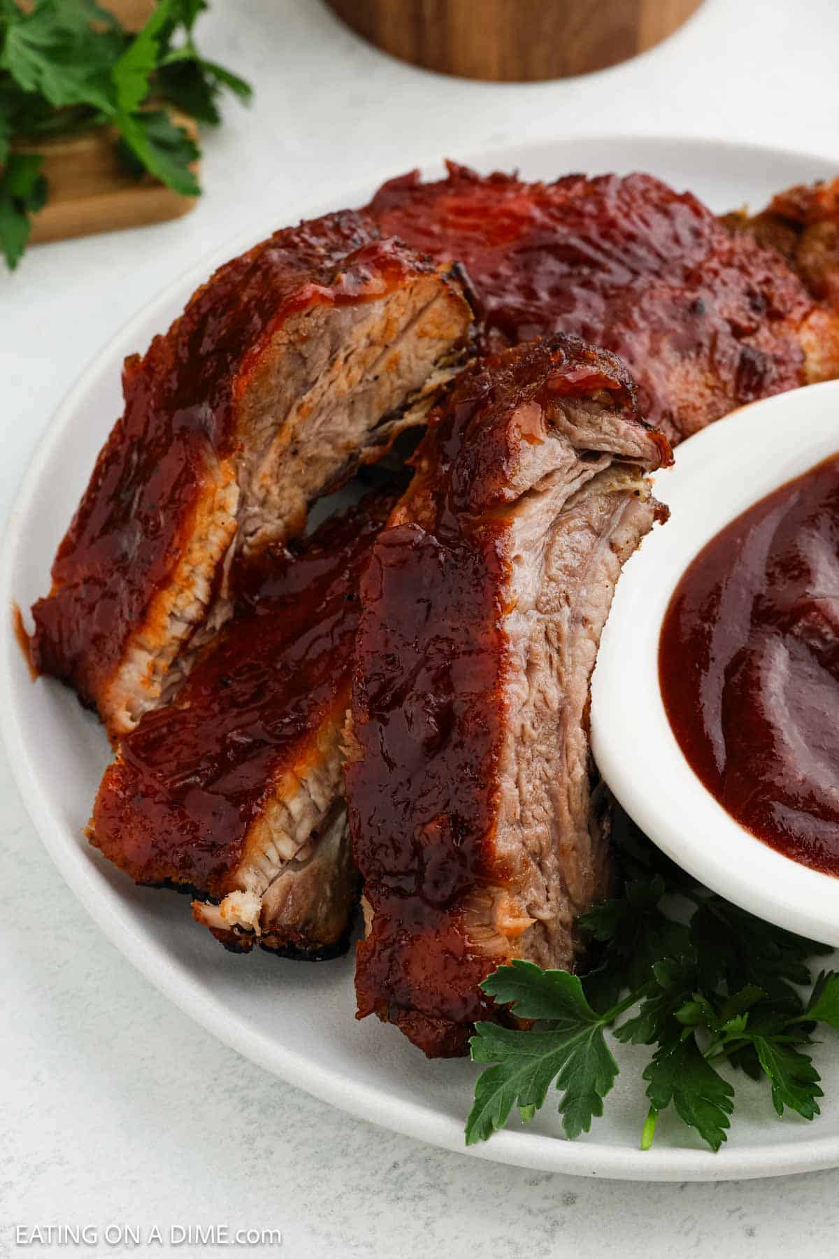 BBQ Ribs Sliced on a plate with a small bowl of BBQ Sauce on the side