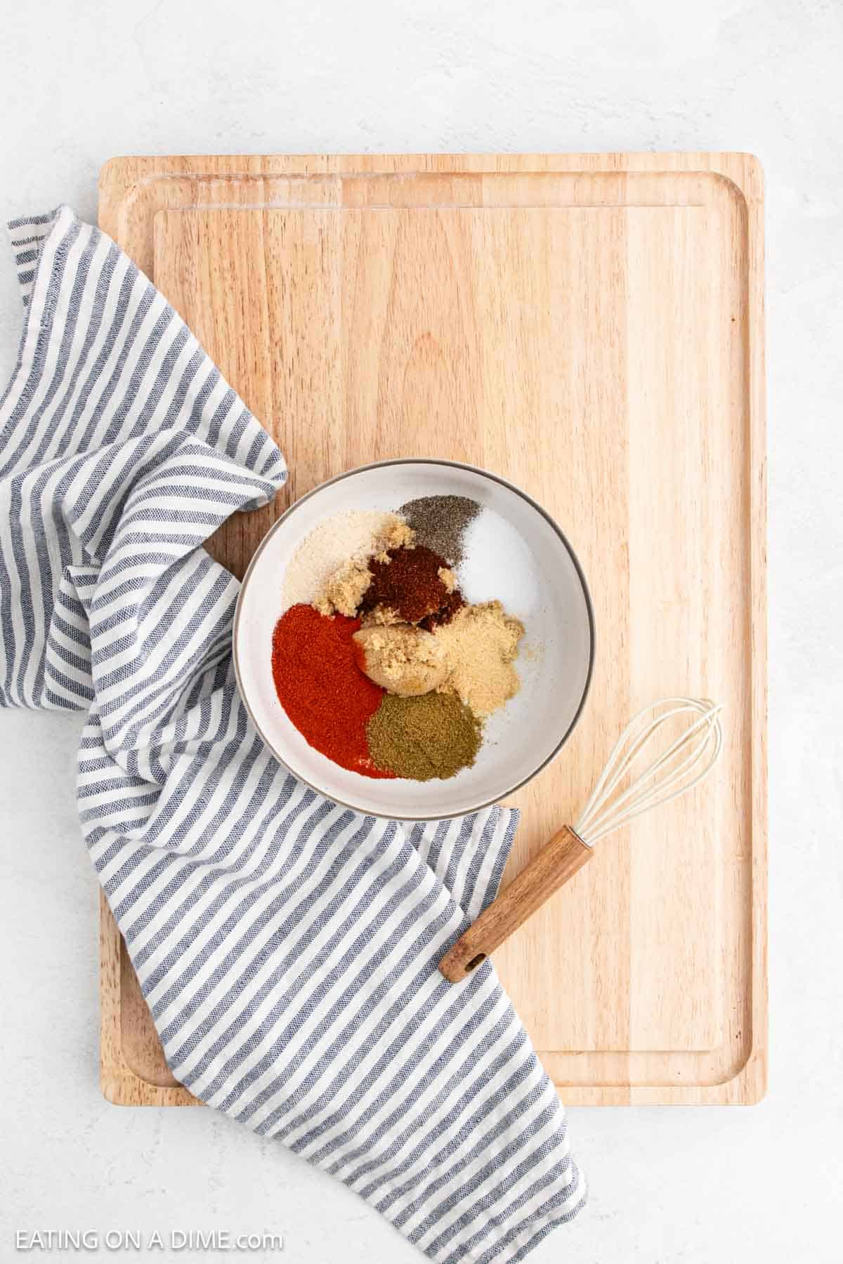 Combining the spices in a bowl on a cutting board with a whisk on the side