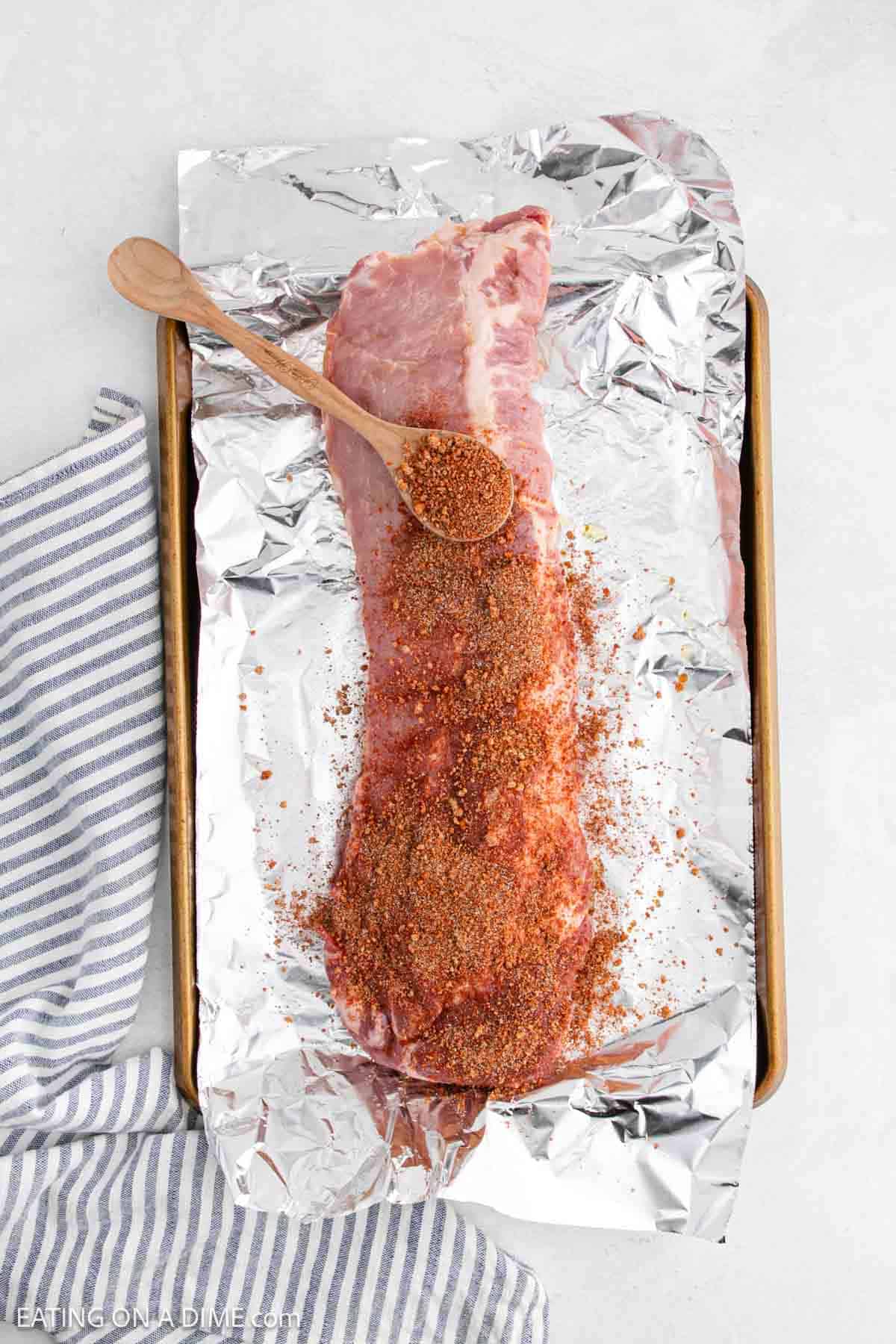 Uncooked baby back ribs on a foil lined baking sheet topped with seasoning blend