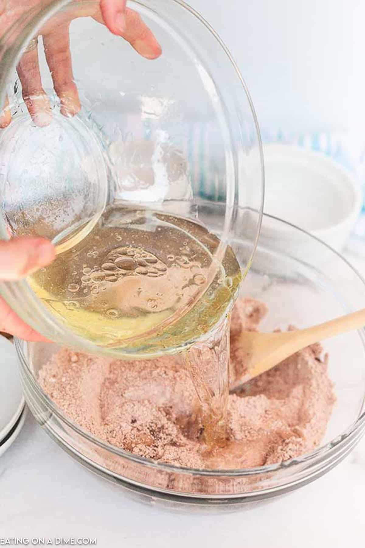 Pouring the oil mixture into the cocoa powder mixture in a bowl with a wooden spoon